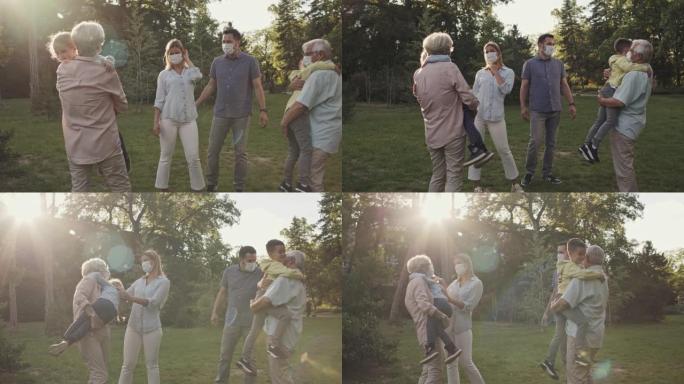 父母和他们的两个孩子与祖父母见面，在公园拥抱