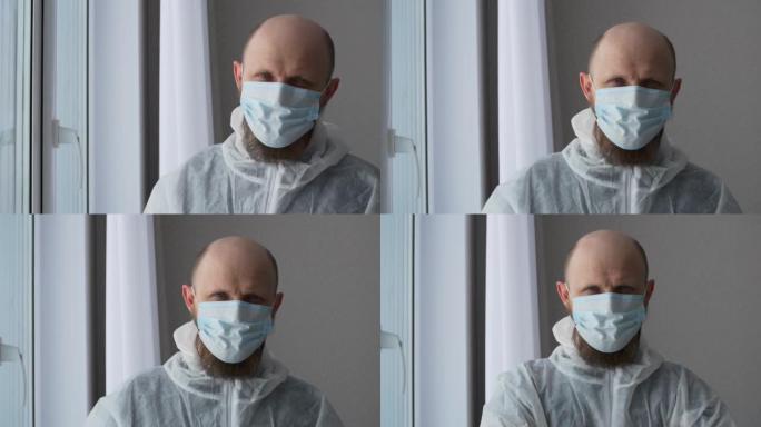 一位男医生戴着口罩和防护服站在窗前。大流行期间医生的生活。在医院中抗击危险疾病的英雄