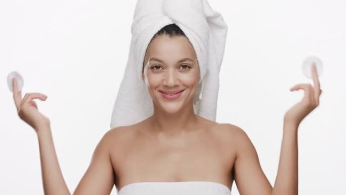 头发上有毛巾的女人用棉垫遮住眼睛，微笑