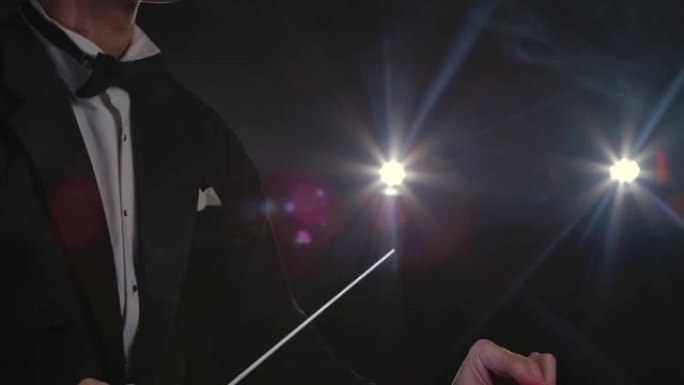 管弦乐队指挥的动手指导音乐家，指挥指挥棒在黑色背景上的灯光下移动。用可见的手势指挥、指挥古典音乐表演