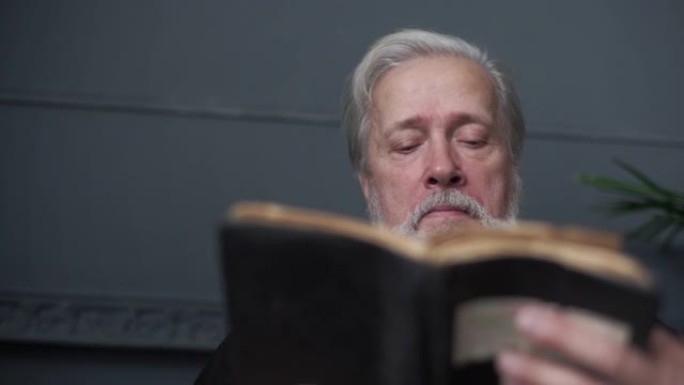 专注的大胡子老人阅读手持旧纸质书的特写低角度视图。