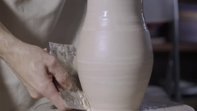 陶工的男性手使用陶器工具形成一个柔软的白色陶罐，在创意车间将其转动到陶工的轮子上。主人给陶器一个形状