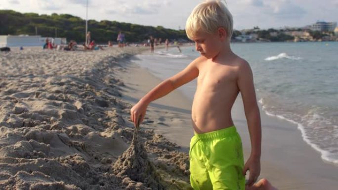男孩用潮湿的沙子、沙滩、大海建造雕像。佛克斯注意落粒落沙。