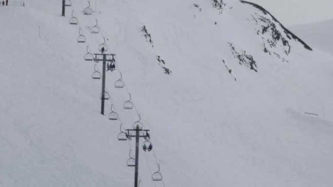 滑雪者从陡峭的斜坡上下来，而其他在升降椅上的滑雪者则在斜坡开始的高原上领先