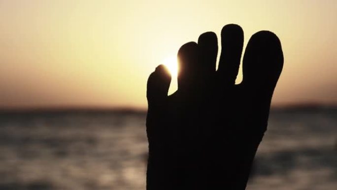 日落时躺在海边沙滩上的年轻人脚的POV剪影
