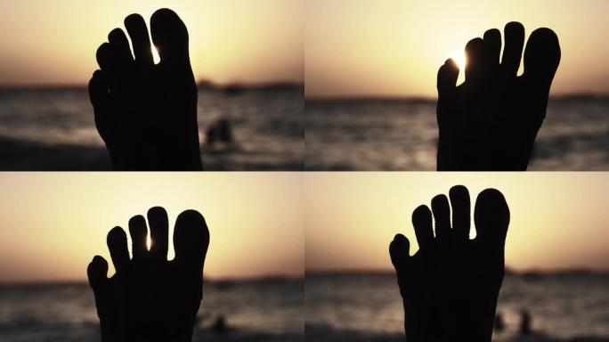 日落时躺在海边沙滩上的年轻人脚的POV剪影