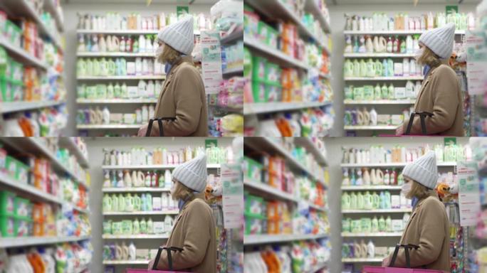 穿着外套和口罩的女人在商店里选择洗衣产品。