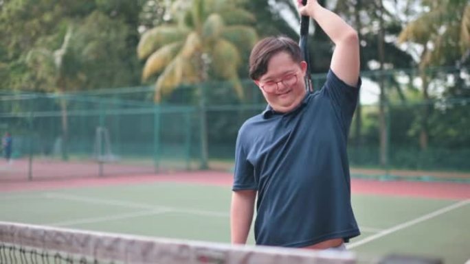 亚洲华人唐氏综合症在网球场微笑着用网球拍挠背