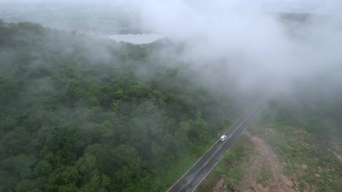 空中无人机电影拍摄的汽车和道路在早上下雨后越过山顶，有雾和绿色森林。