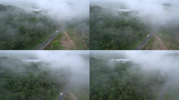 空中无人机电影拍摄的汽车和道路在早上下雨后越过山顶，有雾和绿色森林。