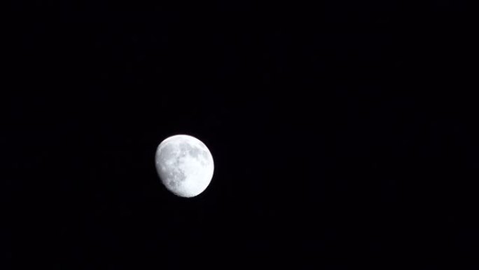 长视频的近景逐渐消失，灰色的月亮从左到右在全黑的天空中移动，出现在左侧，超出摄像机视图水平移动，消失