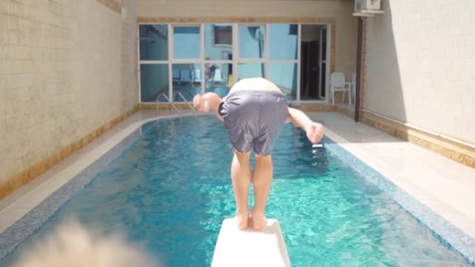 男子跳进游泳池后视图。跳入游泳池的水中，飞溅