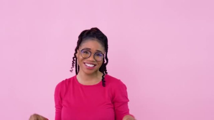 穿着粉色衣服的非洲裔美国女孩玩得开心，用带把手的纸层压袋跳舞。十几岁的女孩站在坚实的粉红色背景