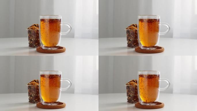 Rooibos茶在透明的玻璃保温瓶中冲泡，以保持热量。泡茶过程的可视化。茶叶绕一圈的运动。桌子上的杯