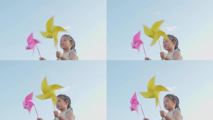 亚洲儿童女孩玩风车，快乐小女孩微笑在麦田里拿着小风轮或风车玩具在公园花园的夏日