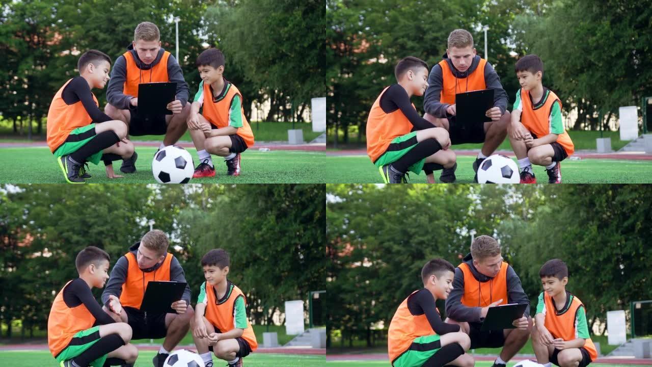 乌克兰利沃夫-7月3日。经验丰富的年轻足球教练的前视图，在足球场上训练时向两名初级球员解释了比赛模型