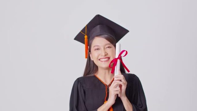 美丽迷人的亚洲女人毕业于帽子和礼服微笑，手里拿着认证的感觉如此自豪和幸福，孤立在白色背景上，教育成功