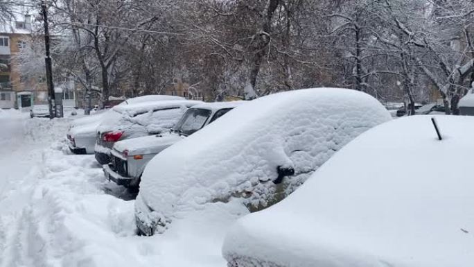 跟踪在院子里严冬风暴下被雪覆盖的汽车的照片。雪在街道和汽车上漂移。