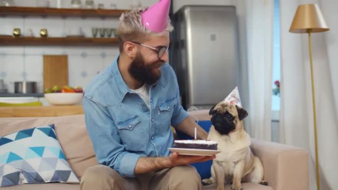 嬉皮士和可爱的哈巴狗坐在沙发上吹熄蛋糕上的蜡烛