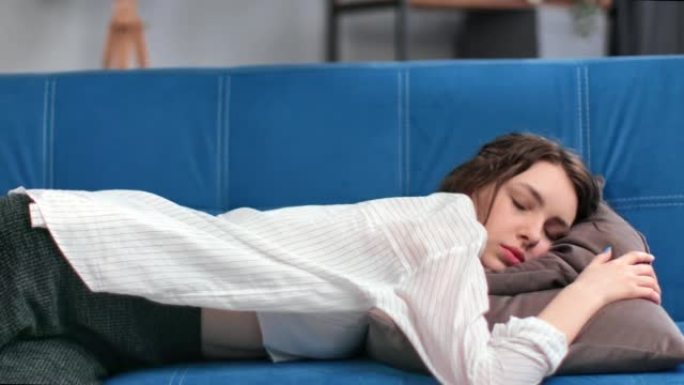 疲惫的黑发女人摔倒在舒适的靠垫蓝色沙发上，精神疼痛过度劳累