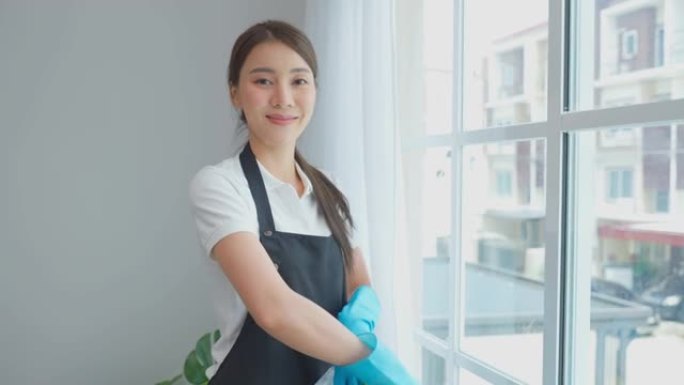 在客厅工作的亚洲清洁服务女工肖像。漂亮的女孩家庭主妇管家清洁工感到快乐，擦窗户做家务或家务，然后看相