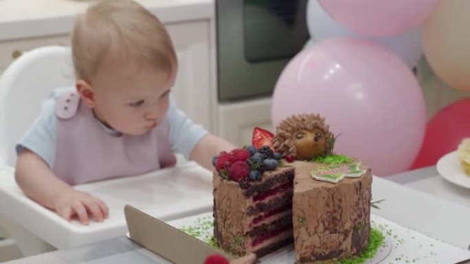 婴儿庆祝第一个生日假期，可爱的小孩试图到达蛋糕，一岁的孩子在他的第一个生日聚会上面对五颜六色的气球。