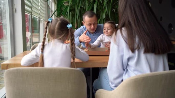 一个大家庭正坐在咖啡馆里吃披萨。父亲母亲和两个女儿在一起度过