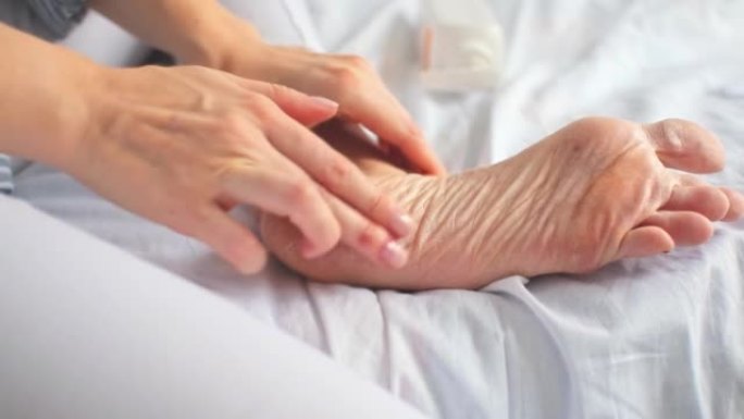女人坐在白色的床上，用手在干裂的脚后跟涂抹保湿滋养霜。家脚护理。