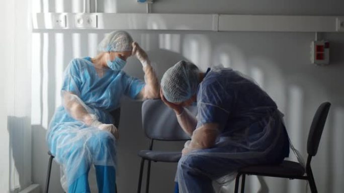 穿着无菌长袍和安全面罩的疲惫的外科医生坐在病房的椅子上休息