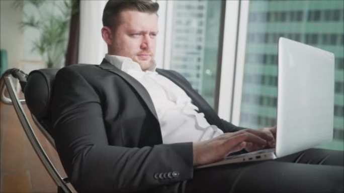 商人躺在舒适的椅子上，腿上放着笔记本电脑山毛榉。男人微笑着坐在笔记本电脑上。为IT公司做广告。经理的