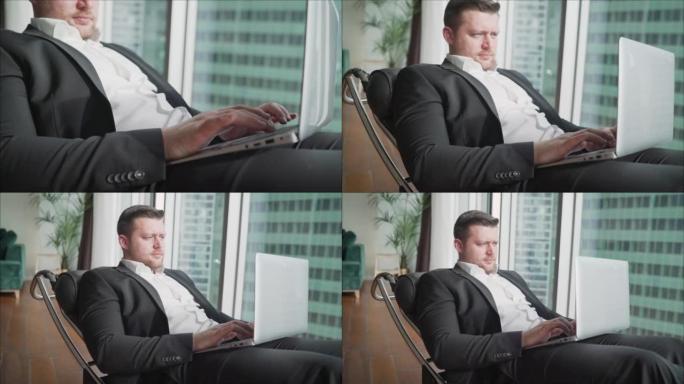 商人躺在舒适的椅子上，腿上放着笔记本电脑山毛榉。男人微笑着坐在笔记本电脑上。为IT公司做广告。经理的
