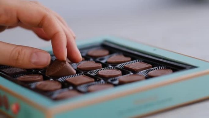 女人从一盒不同的糖果中取出一颗巧克力。特写拍摄素材。慢动作