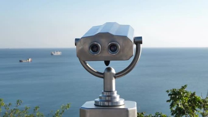 海边的公共双筒望远镜，特写镜头。在日落和大海的模糊背景上的硬币双目观看器