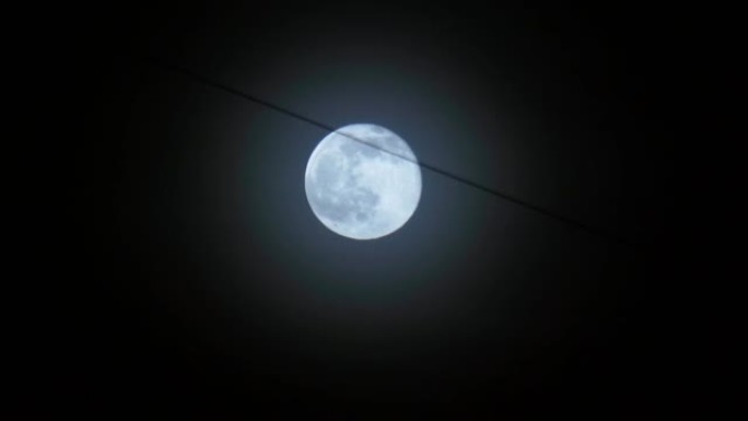 满月在夜空中移动。月光照在黑色的夜空中。夜城的电线