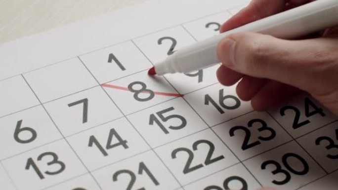 人的手用红笔在纸质日历上写下第23天。