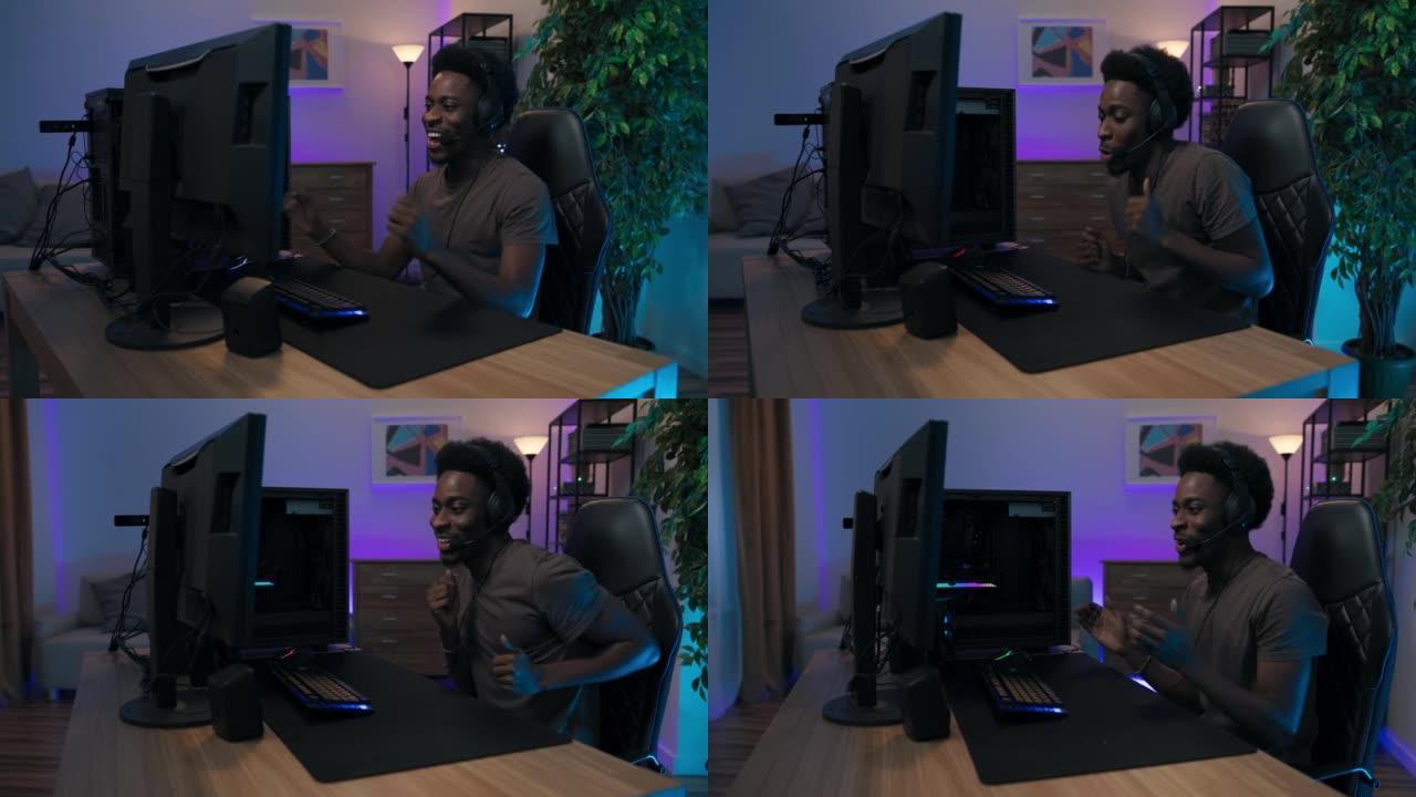 快乐的男玩家坐在电脑前戴着耳机，专业的游戏设备，家伙赢了回合，过关了，胜利用手跳舞