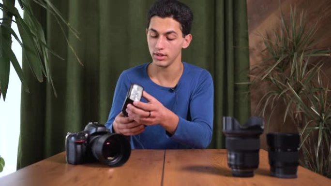 关于如何选择以及如何使用相机的照片闪光灯的视频教程。一个年轻有魅力的阿拉伯男人正在用相机拍摄自己。在