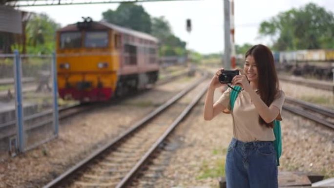 年轻美丽的亚洲女游客用胶卷相机拍照，在火车站平台上微笑和享受，乘坐火车运输度假旅行的快乐旅行生活方式