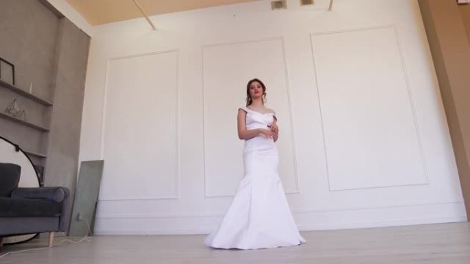 穿着白色连衣裙的快乐新娘站着为摄影师摆姿势。