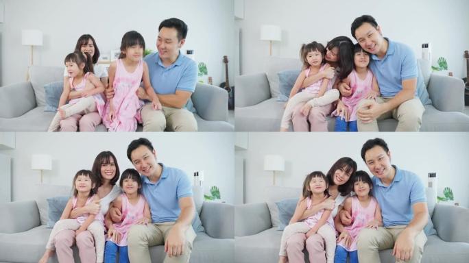 亚洲幸福家庭的肖像和孩子一起呆在家里。年轻可爱的小女孩女儿和父母坐在沙发上微笑，看着客厅的相机。活动
