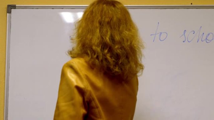 老年女教师在黑板上写作，背景是教室