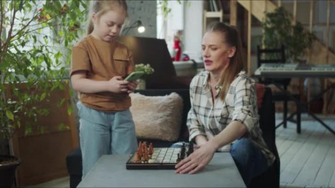 一个女人从孩子那里拿了一部智能手机，这样女孩就可以和她下棋了