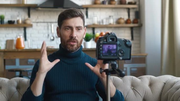 受欢迎的博主男子在家用专业相机拍摄新的vlog视频。男性内容创作者坐在沙发上拍摄在线课程。用摄像机录