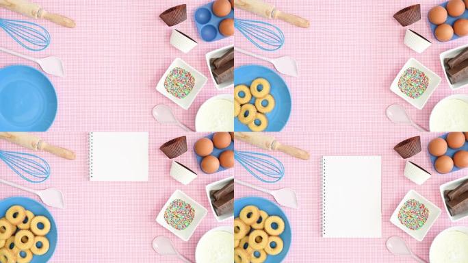 烤盘中的食材和饼干出现在柔和的粉红色背景上，带有空笔记本的食谱。停止运动平铺