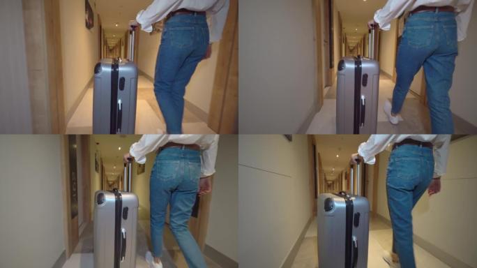 女人走在酒店的走廊上，用轮子上的行李滚动行李箱。