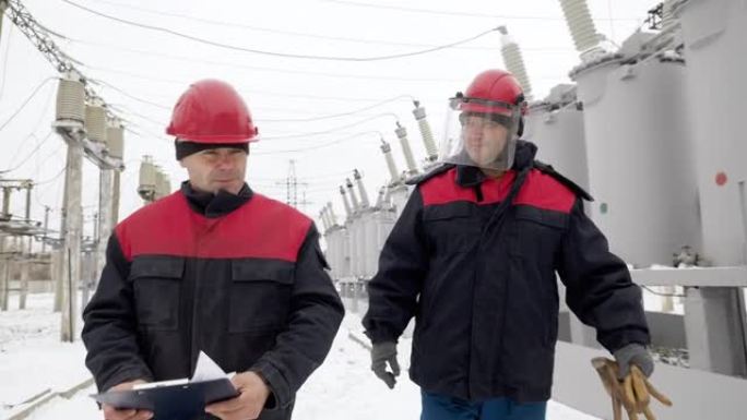 两名穿着防护服的自信男子在冬季户外行走并检查电气设施