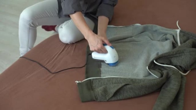 无线设备，用于从棉绒中清洁针织织物。那个女人正在去除毛衣上的棉绒。