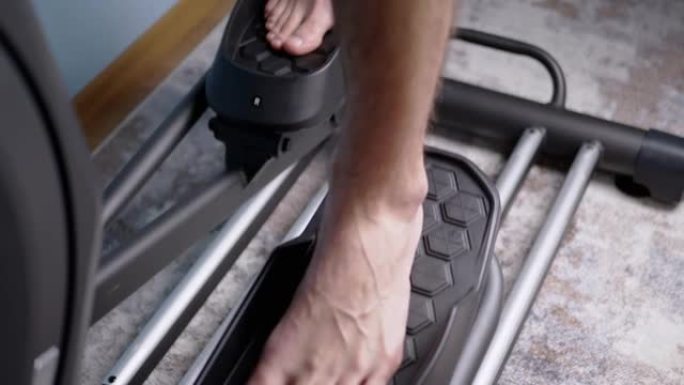 赤脚男性脚在家里的椭圆形交叉训练器模拟器上踩踏板