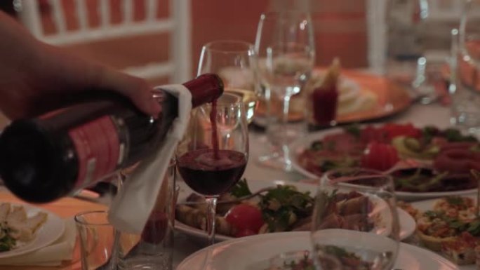 服务员将红酒从酒瓶倒入宴会桌上干净的酒杯中。