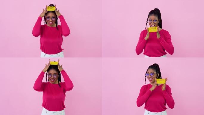 穿着粉色衣服的非洲裔美国女孩拿着一个迷你玩具购物篮。少女家庭主妇初学者站在坚实的粉红色背景上